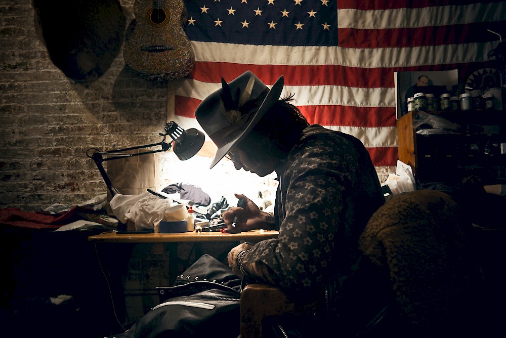 Christian Benner working on a Jacket in front of an american flag in his studio in New York