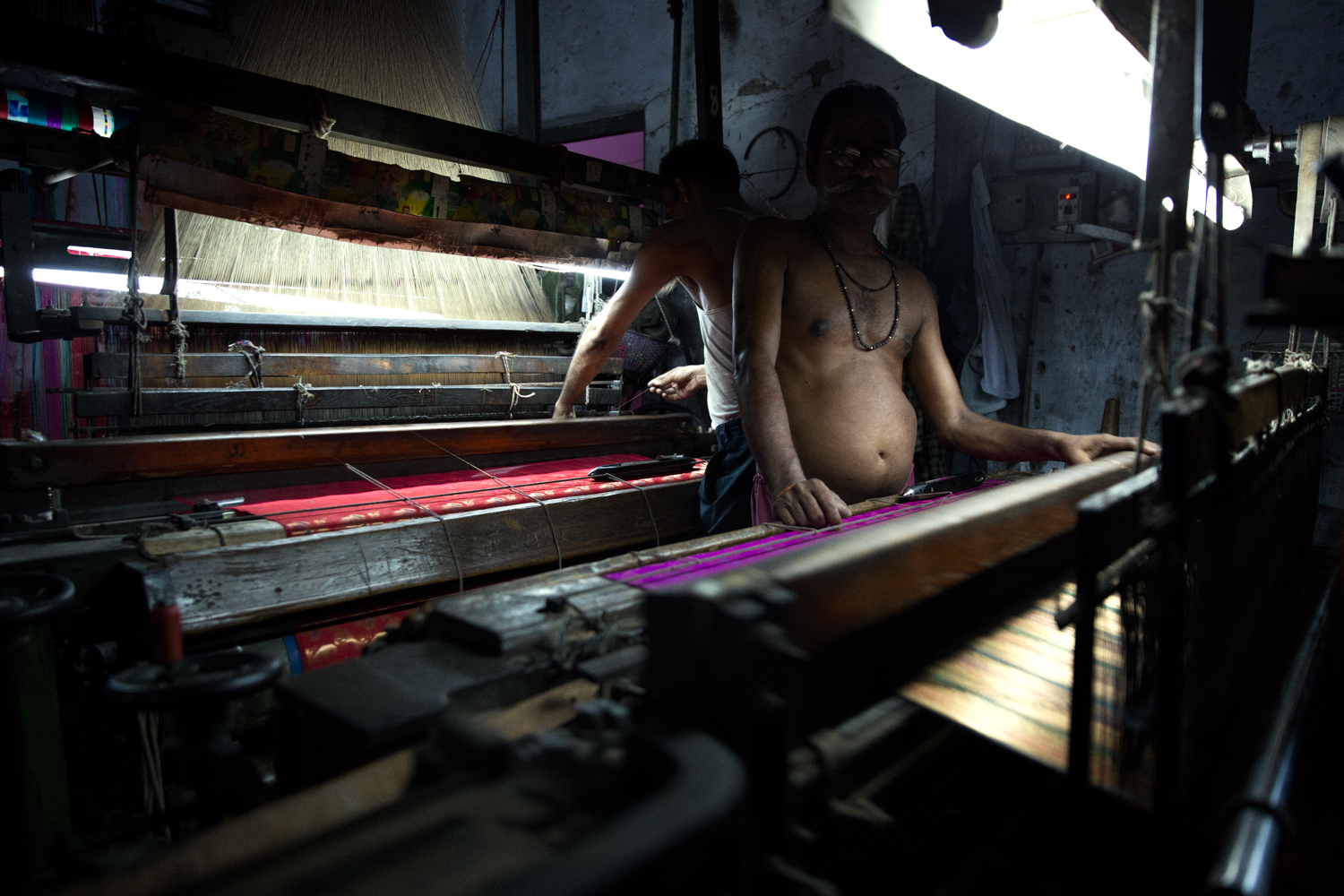 Two indian men standing in front of their powerlooms, starring into my camera