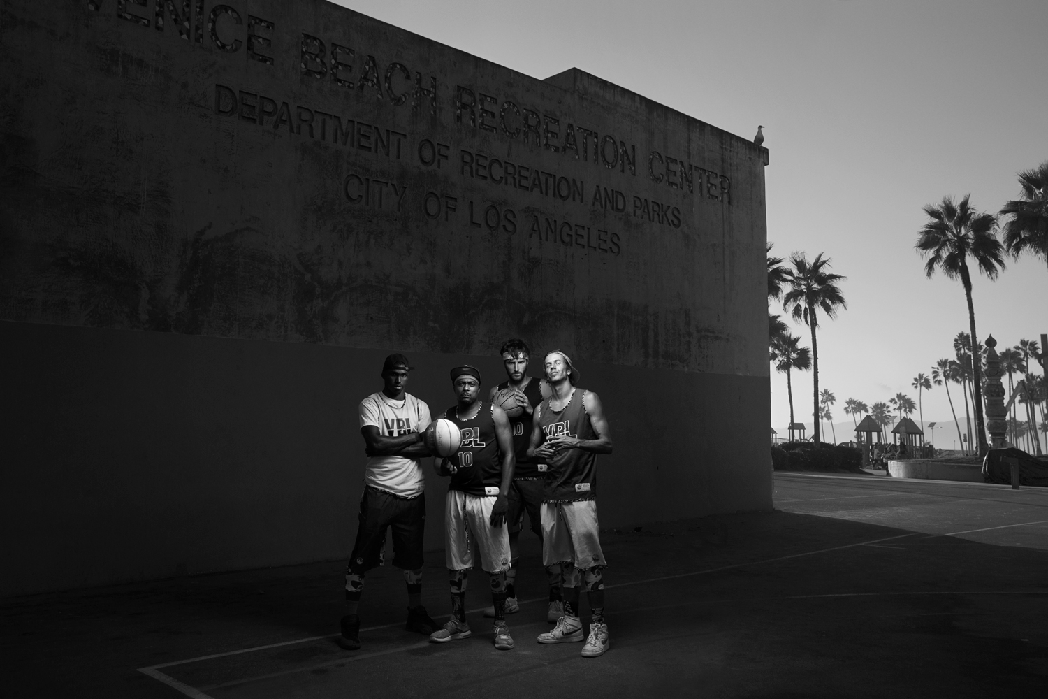 A group picture of young basketball players on a venice beach basketball court with palm trees in the background