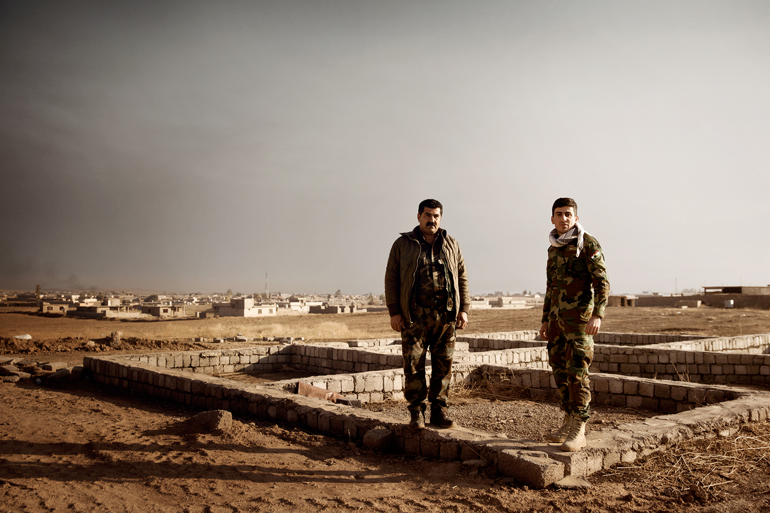 Two Peshmerga soldiers in front of a destroyed town in Kurdistan