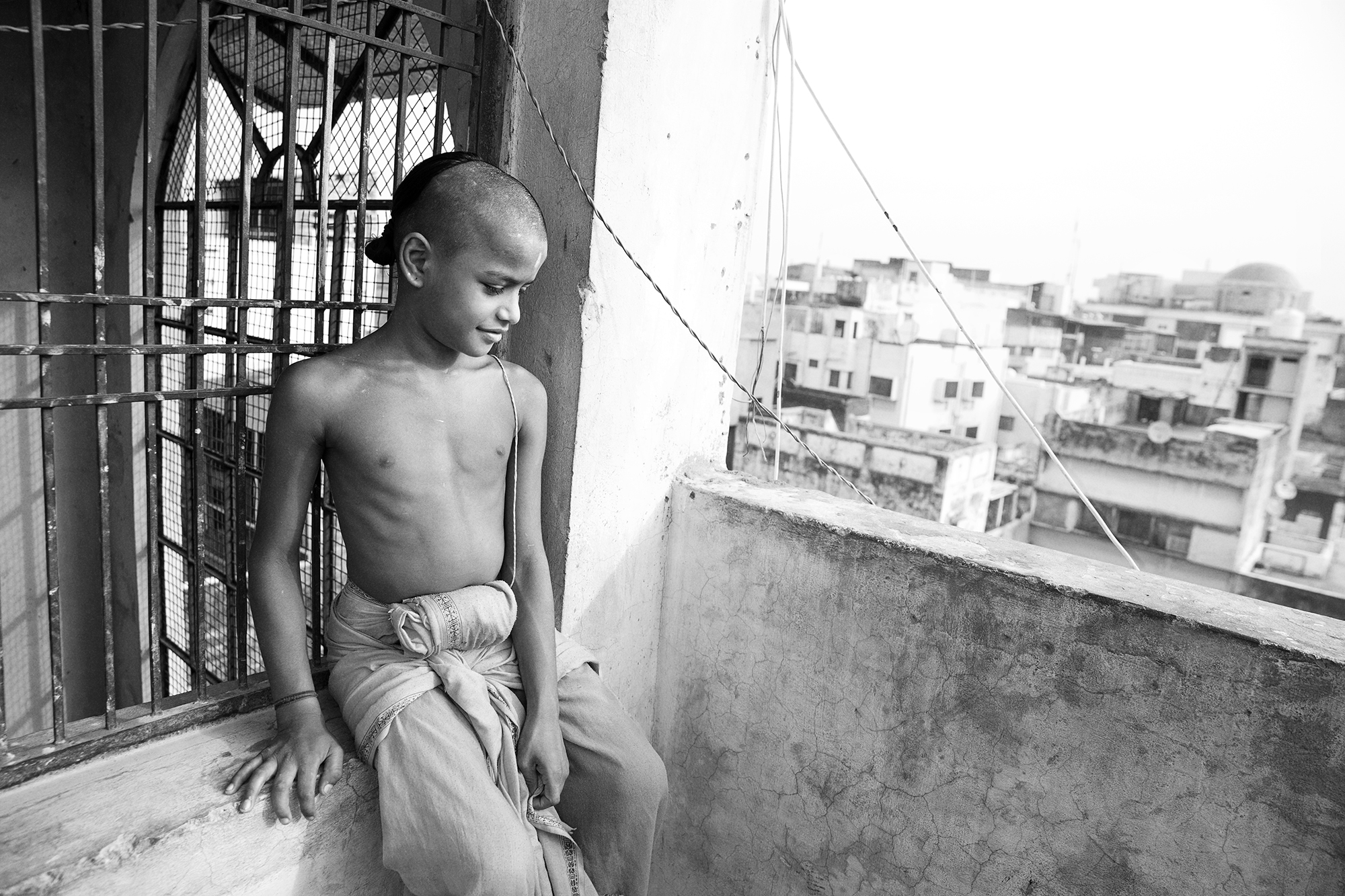 Indian kid is sitting on the edge of the rooftop in Varanasi, India.